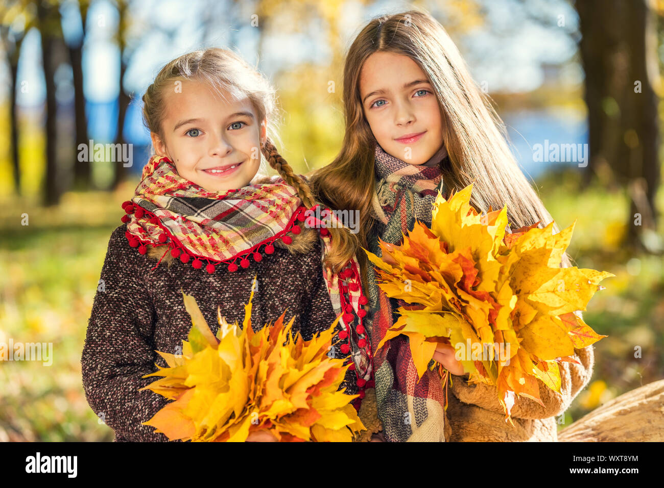 Two cute smiling 8 years old girls posing together in a park on a sunny autumn day. Stock Photo