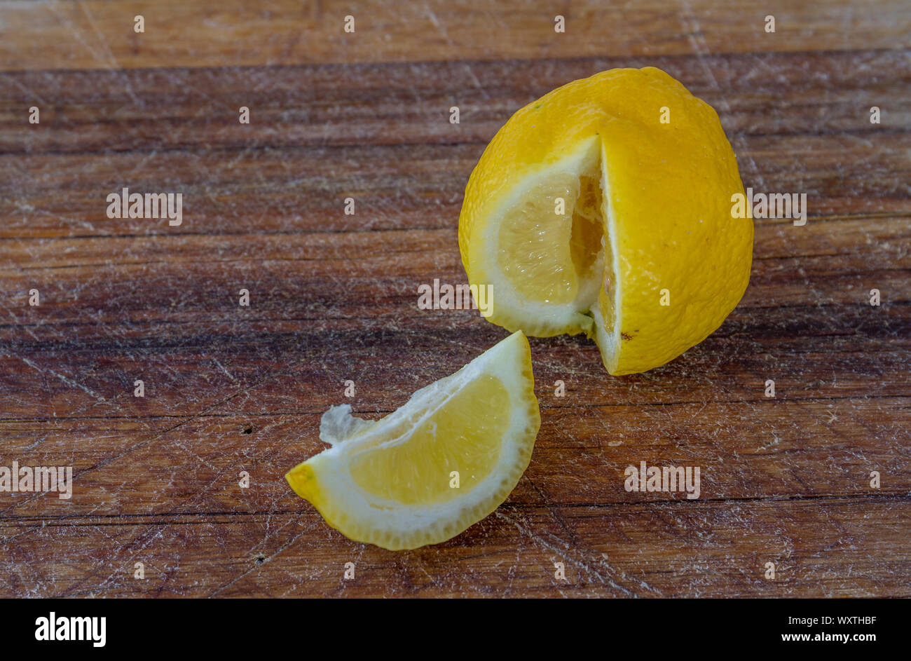 A slice of lemon and the remainder of the fruit isolated on a wooden surface image with copy space Stock Photo