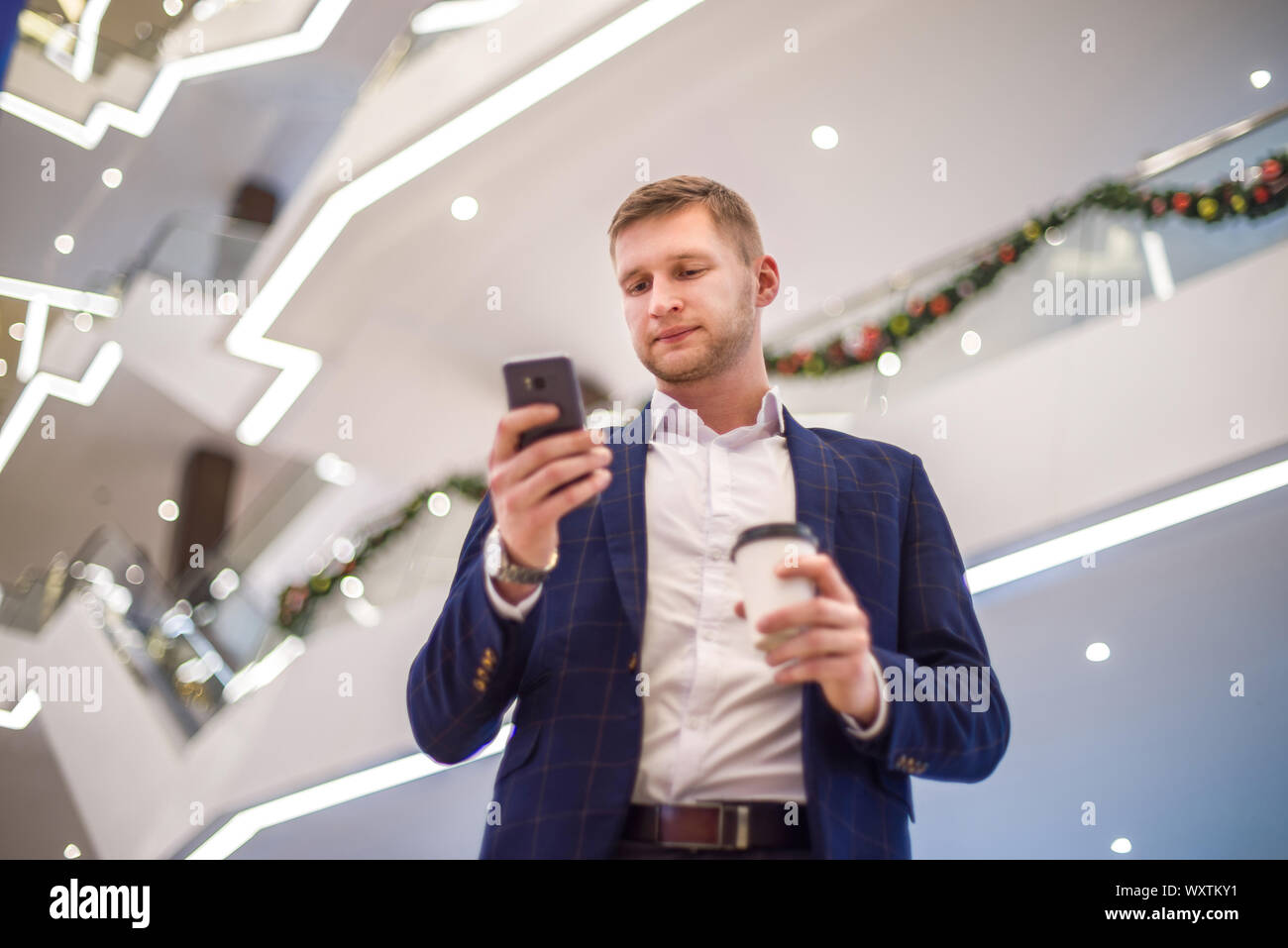 A man dressed in a business style with a glass of coffee looks at his watch. Lunch break. Stock Photo