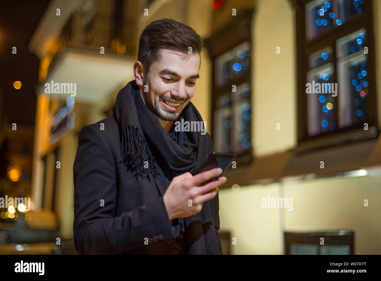 man dressed in business style on the street in the evening looks at the smartphone and smiles. Stock Photo