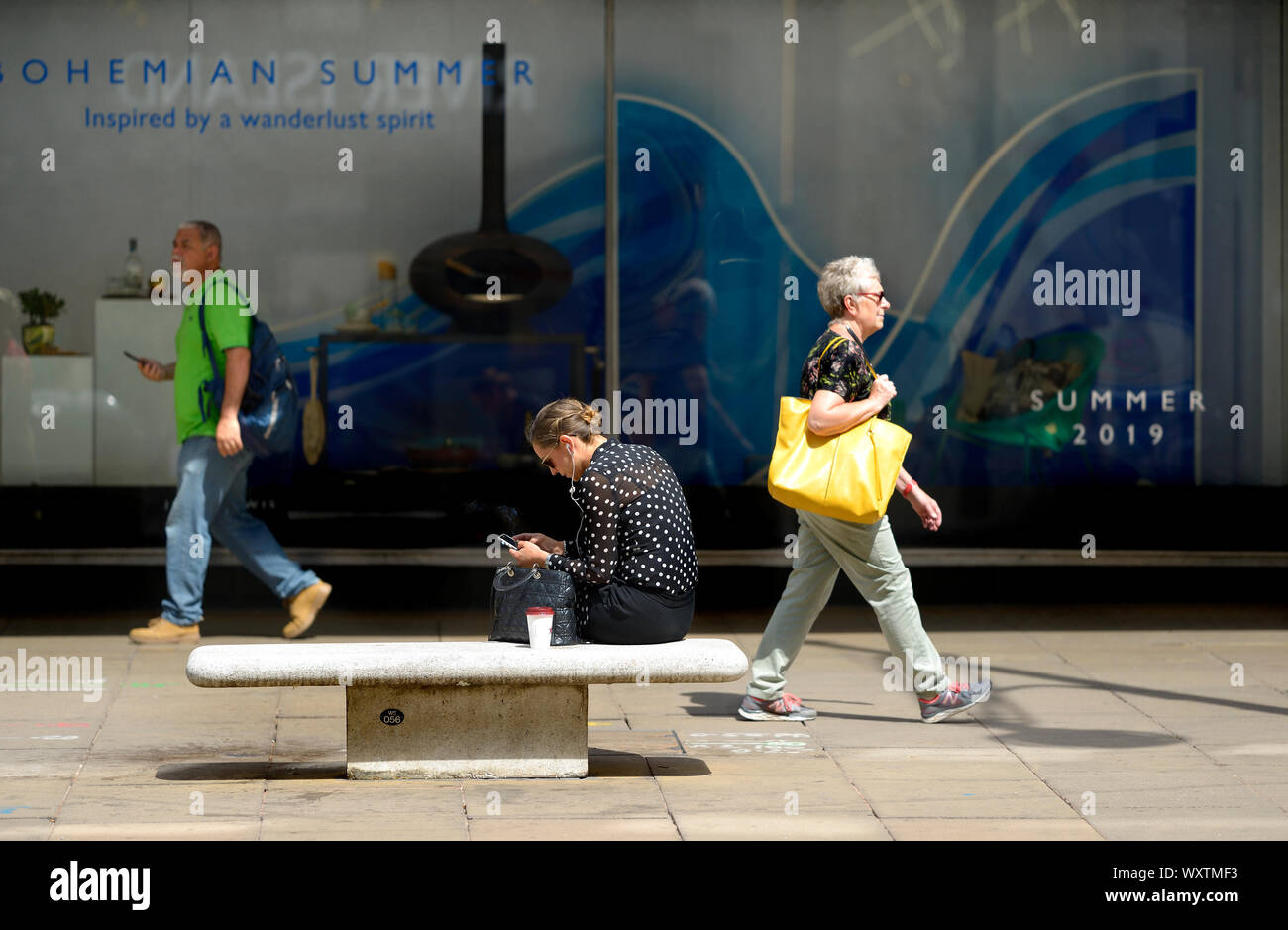 London, England, UK. Woman sitting in Oxford Street looking at her mobile phone and smoking Stock Photo