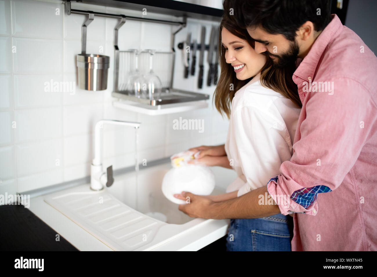 Young couple doing dishes in the kitchen while hugging and having fun Stock Photo