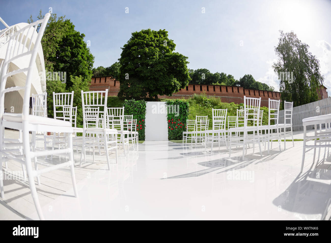 Rows of empty white chairs sitting on a wooden floor. Wedding chairs with flowers at ceremony outdoors Stock Photo