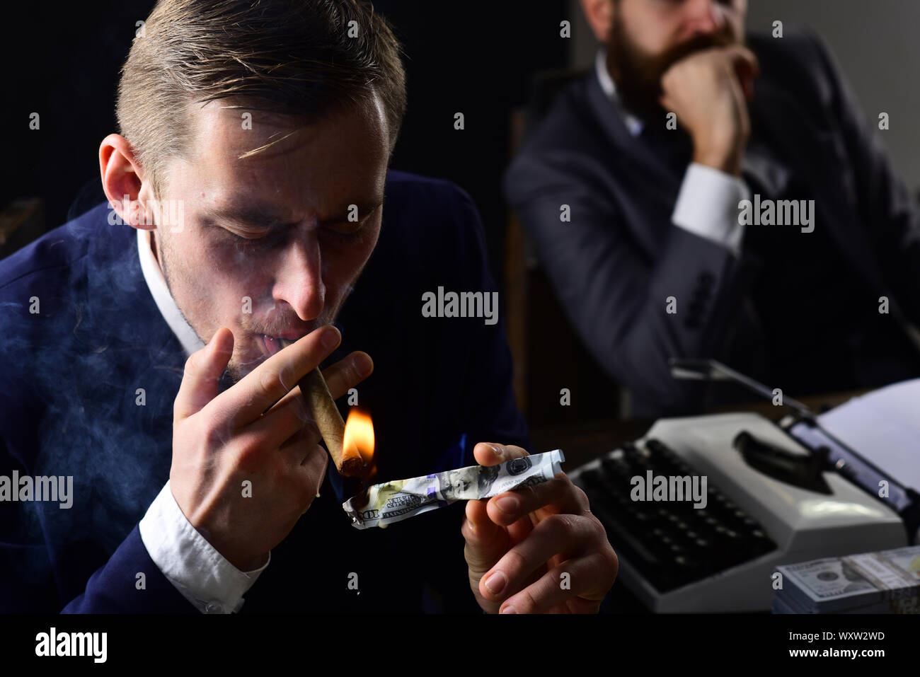 Man lighting cigar from burning banknote. Squander concept. Businessmen