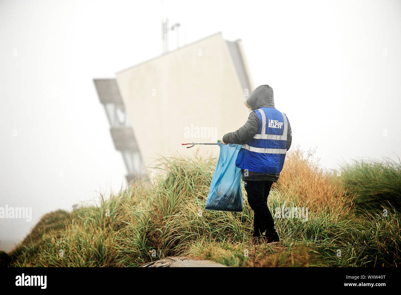 Solitary litter picker working in front of the Rossall Point observation tower on Fleetwood seafront in the wet and cold weather Stock Photo