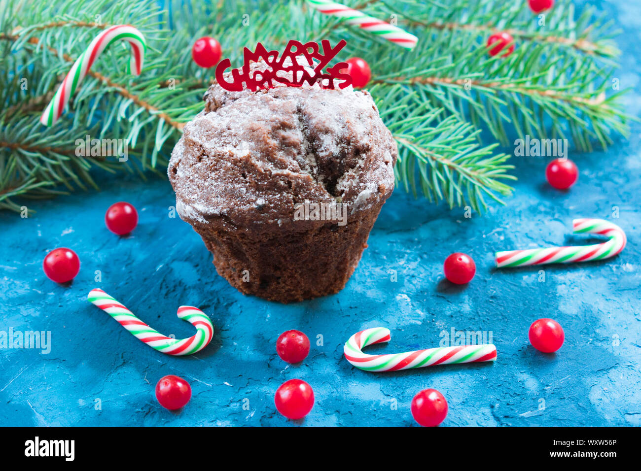 Christmas homemade chocolate muffin decorated with red berries and sweets on the background of a Christmas tree branch. Stock Photo