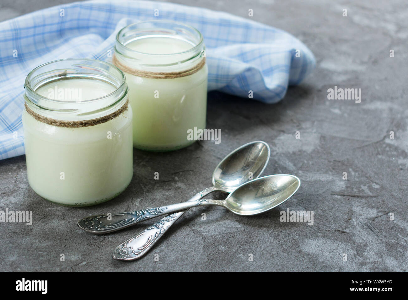 Greek yogurt in glass jars with spoons on a gray textural background