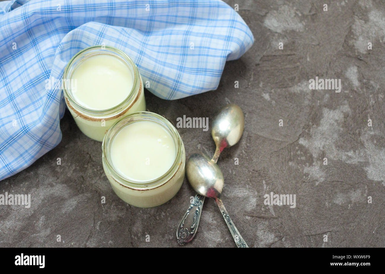 Greek yogurt in glass jars with spoons on a gray textural background