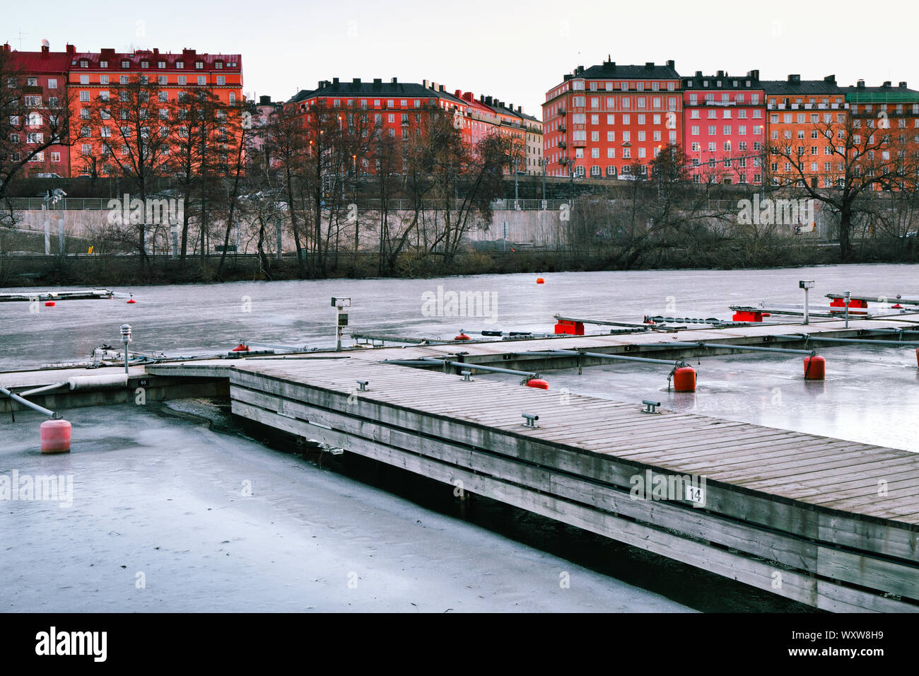Boat moorings frozen in the ice of Karlberg Lake (Karlbergssjon) with colourful facades of the Atlas district houses, Norrmalm, Stockholm, Sweden Stock Photo