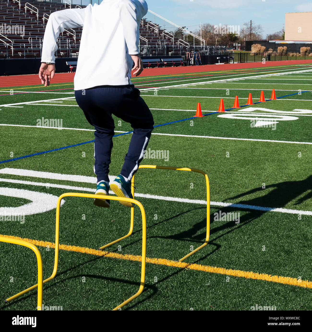 A high school track and field runner is jumping over hurdles during jumps practice on a turf field. Stock Photo