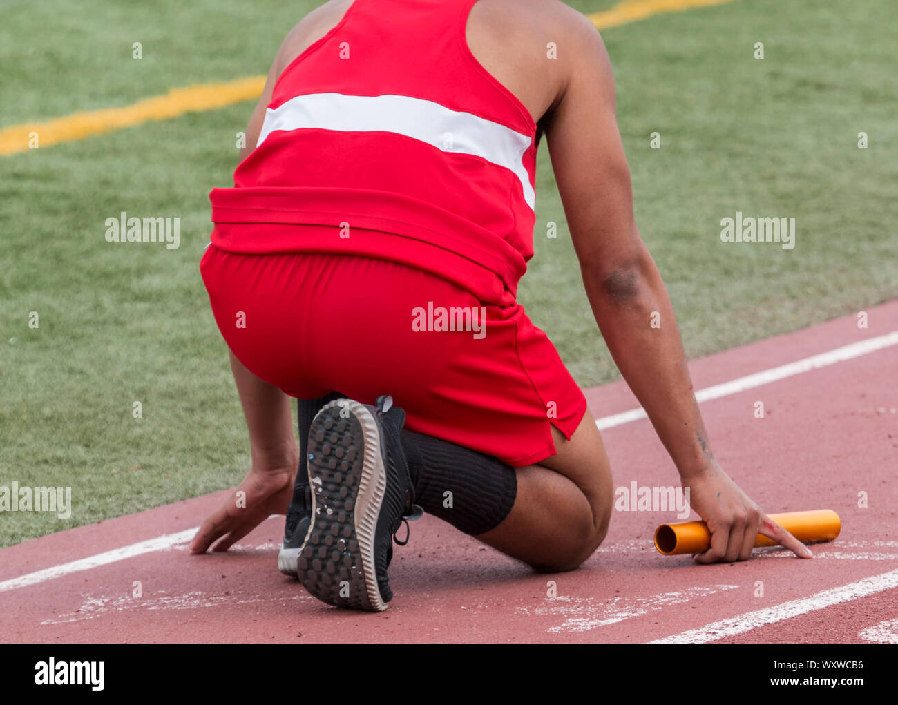 A high school runner is in the on your mark position ready to start a relay race at a track and field competition. Stock Photo