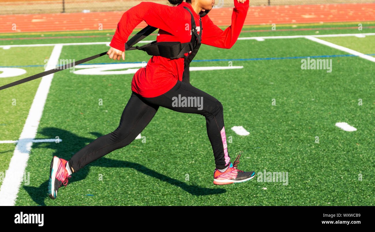 A high school track and field girl is pulling a weighted sled across a green turf field at practice. Stock Photo