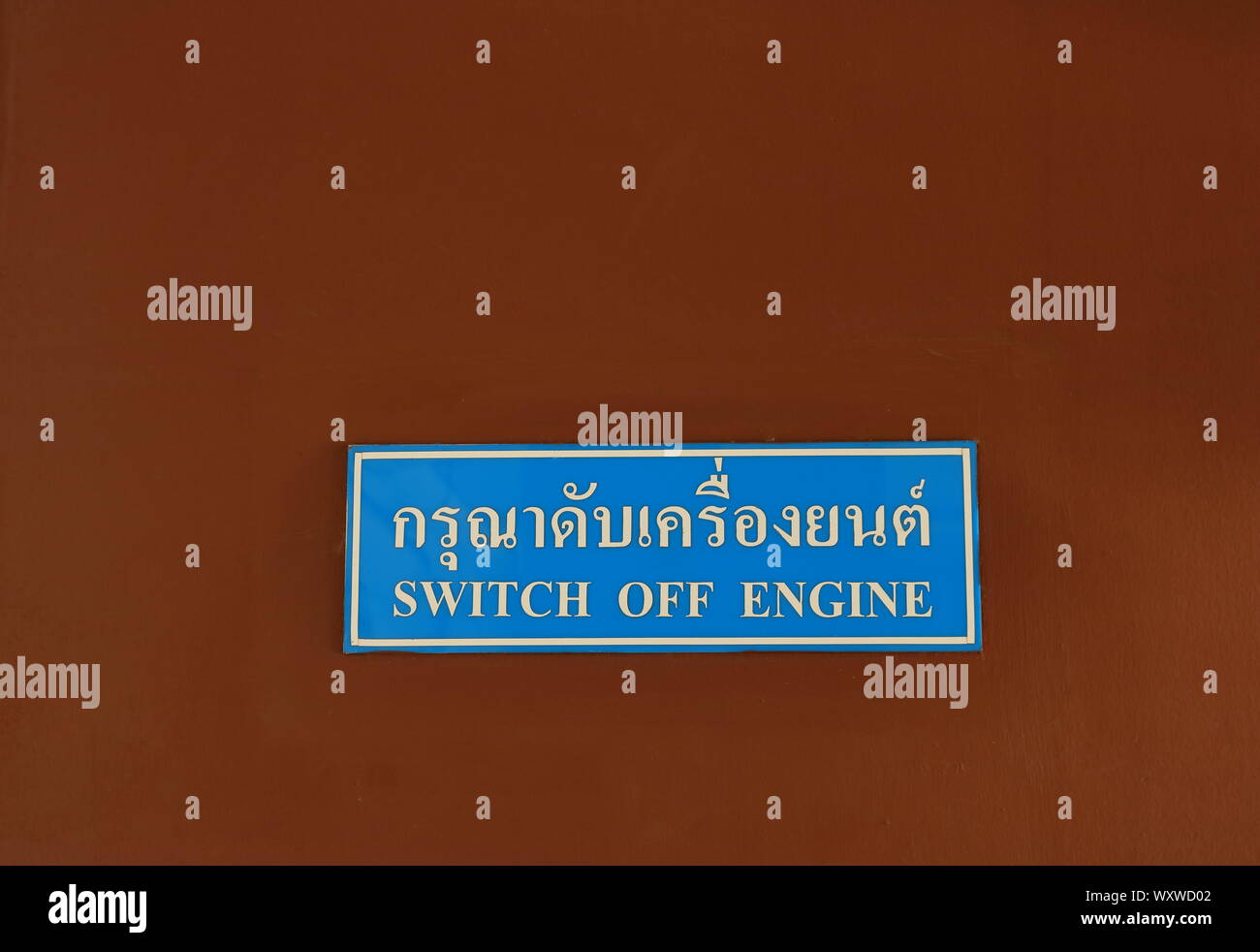 Closeup rectangular sign installed on the wall read switch off engine in both Thai and English language Stock Photo