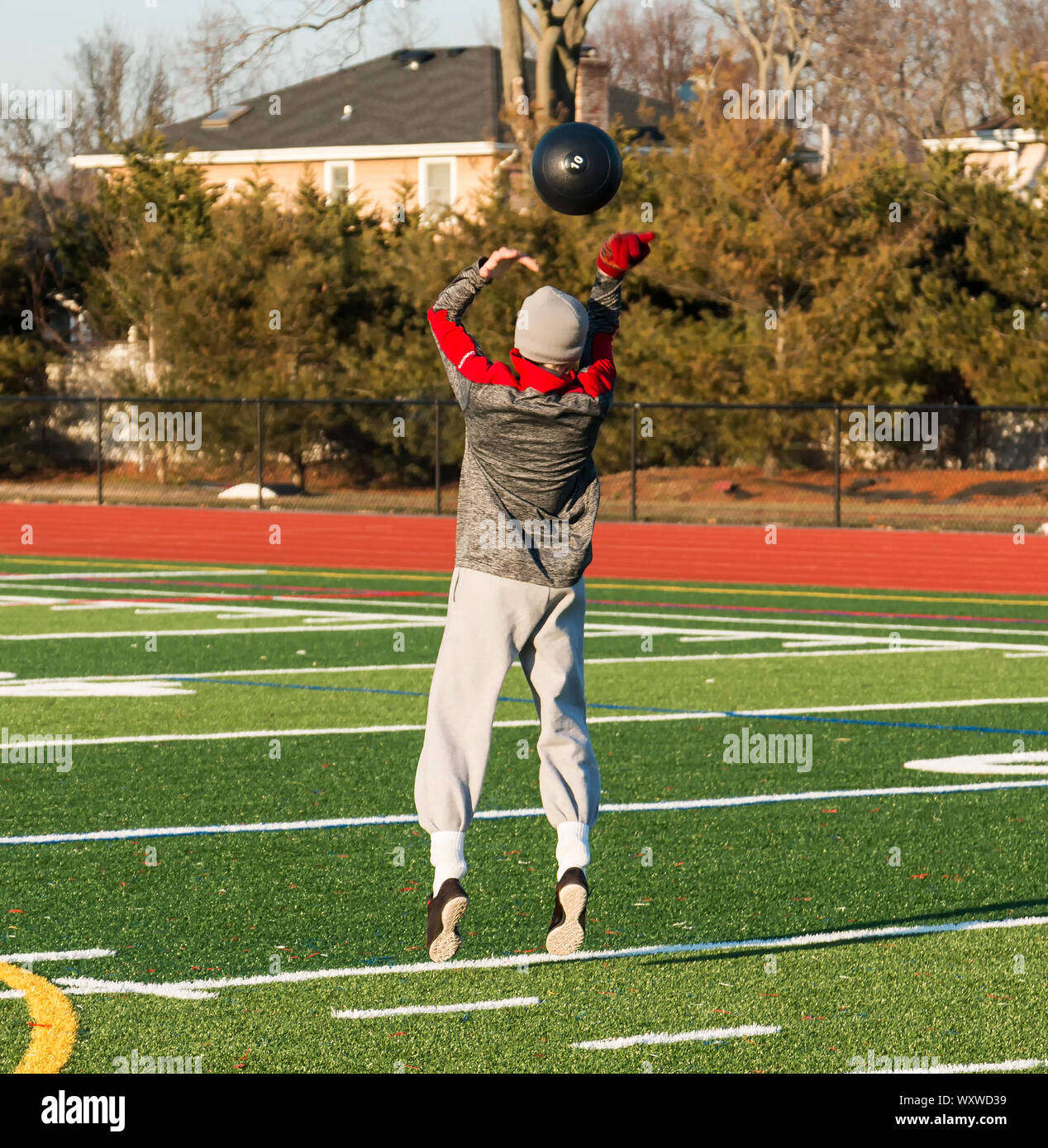 A high school track and field athlete is training for strength and speed by throwing a 10 pound medicine ball over his head while jumping outside on a Stock Photo
