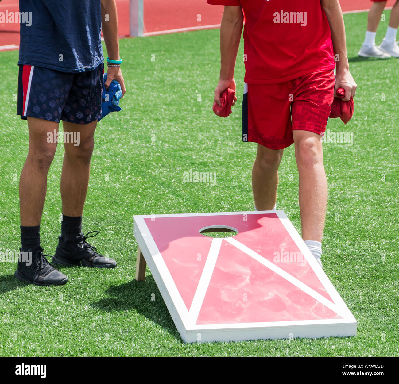 Two boys play corn hole during gym class on a green turf field in the sunshine. Stock Photo