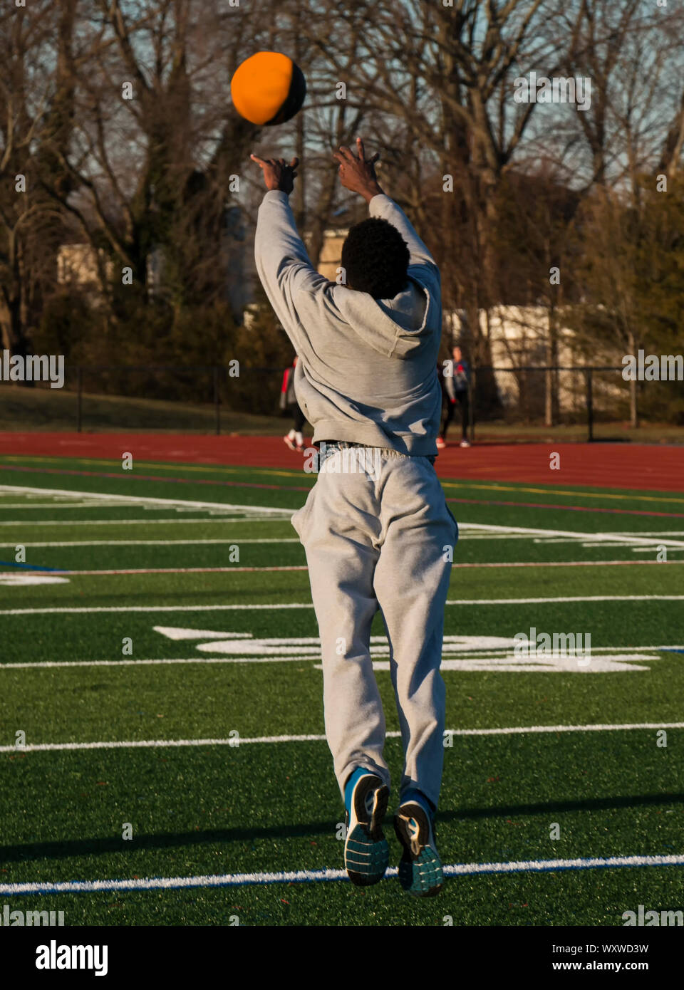 An African american male track and field athlete is tossing a medicine ball forward as he jumps forward as part of strength and speed training. Stock Photo