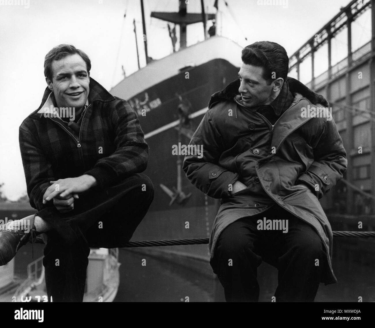 MARLON BRANDO with his stand-in CARL FIORE on set location candid filming ON THE WATERFRONT 1954 director ELIA KAZAN original story / screenplay Budd Schulberg producer Sam Spiegel Horizon Pictures / Columbia Pictures Stock Photo