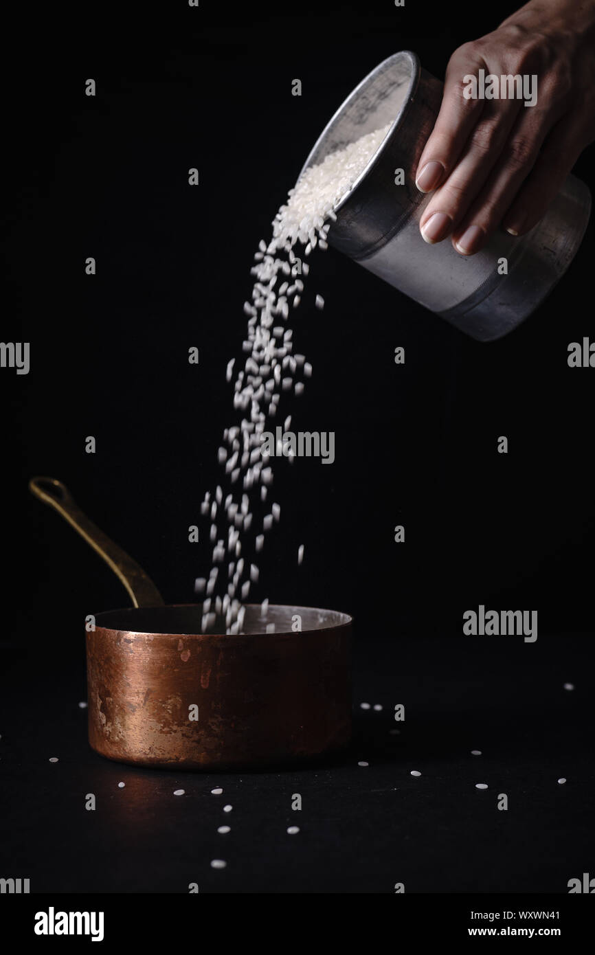 Female hand pouring arborio rice to copper saucepan for boiling. Dark background, copy space