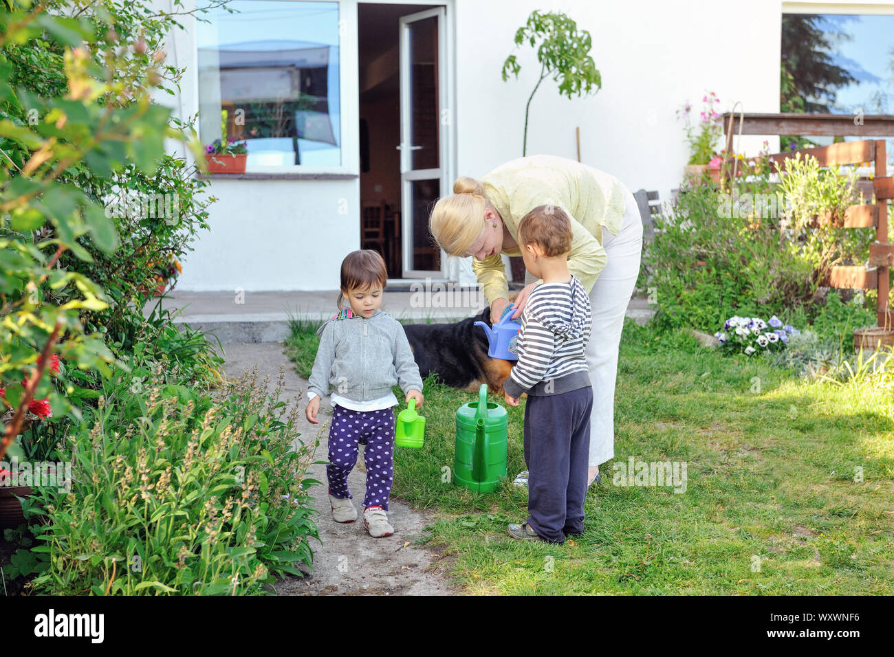 Grandmother with grandchildren watering plants. Summertime. Stock Photo