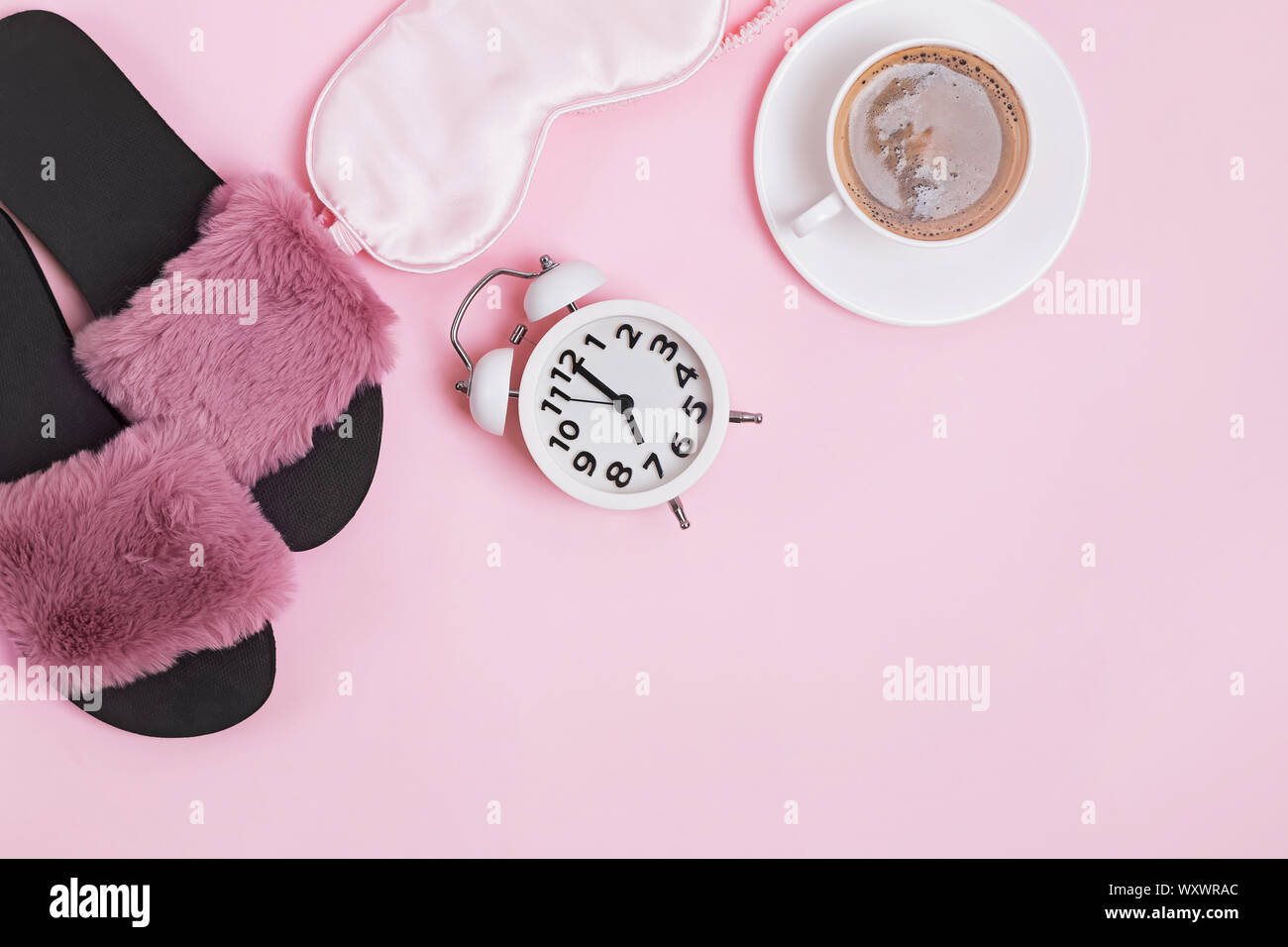 Cozy morning at home. Coffee, sleeping mask, slippers and alarm clock on pink background Stock Photo