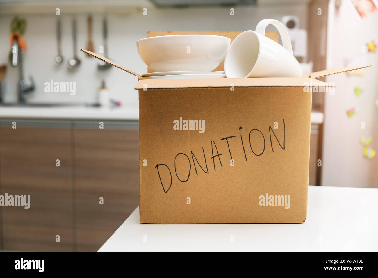 donate household items - box with tableware for donation on kitchen table Stock Photo