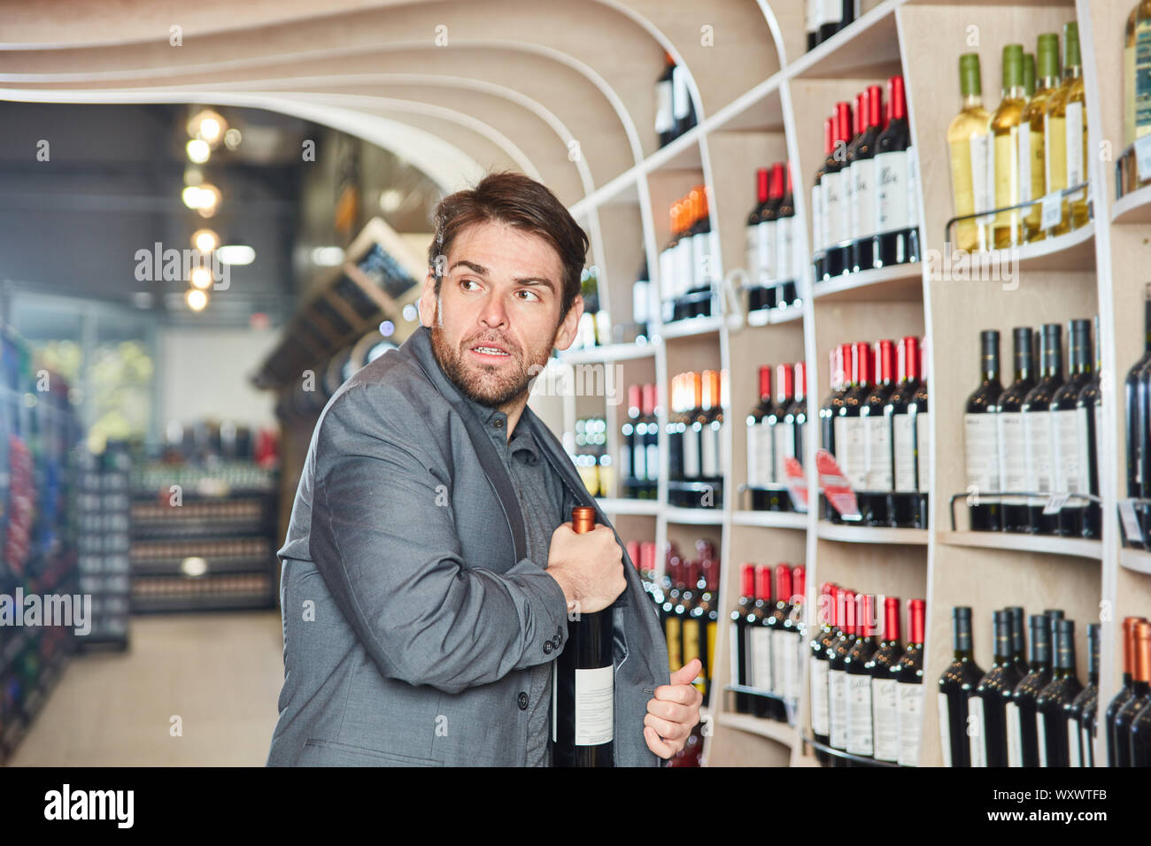 Young man puts a bottle of wine in his jacket during shoplifting Stock Photo