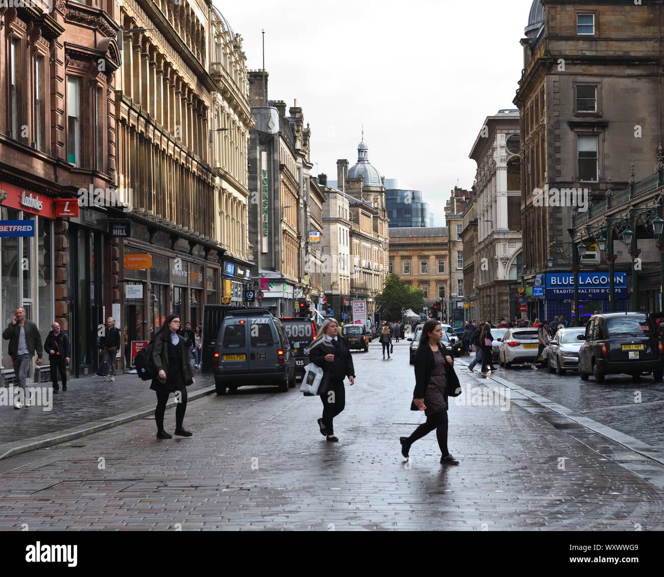 City view of people crossing the wet cobbled road looking east on Gordon Street in Glasgow, Scotland, UK Stock Photo