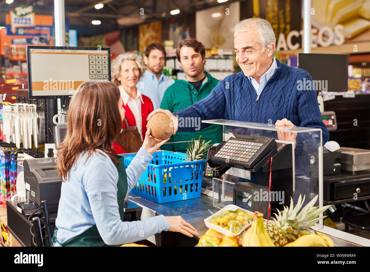 Senior as a friendly customer when paying at the supermarket cashier Stock Photo