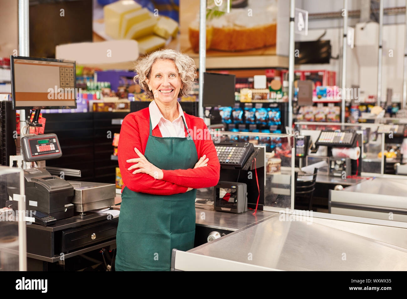 Woman as a cashier or saleswoman stands with folded arms at the cash register Stock Photo