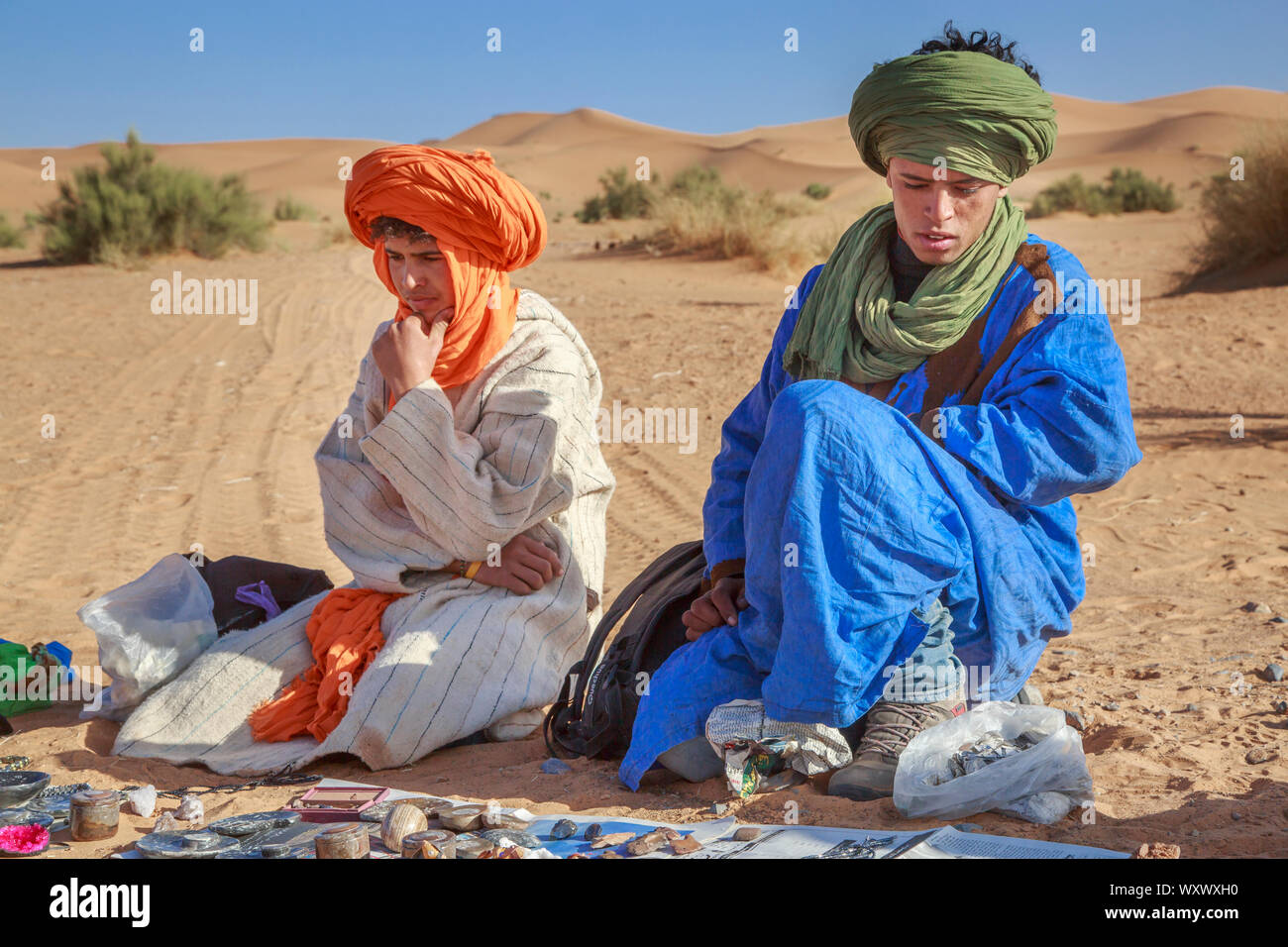 Merzouga, Morocco - February 25, 2016: Nomad souvenir vendors of the Sahara desert dressed in colorful robes and turbans, sitting on the sand under a Stock Photo