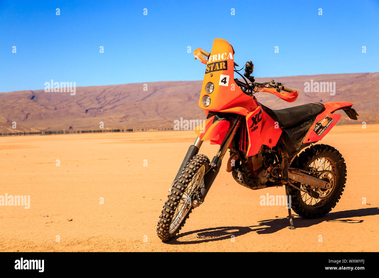 Merzouga, Morocco - February 22, 2016: A single orange motorbike sits alone  on a flat stretch of sand in the Sahara desert under a blue sky with a lar  Stock Photo - Alamy