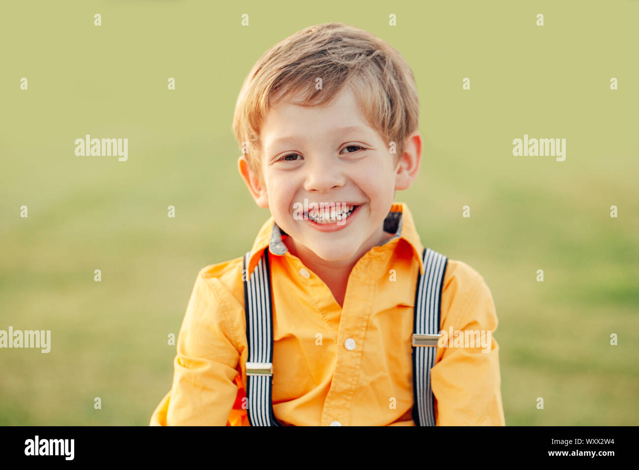 Closeup portrait of funny cute adorable nice smiling laughing Caucasian preschool boy looking in camera against light green background outdoor Stock Photo