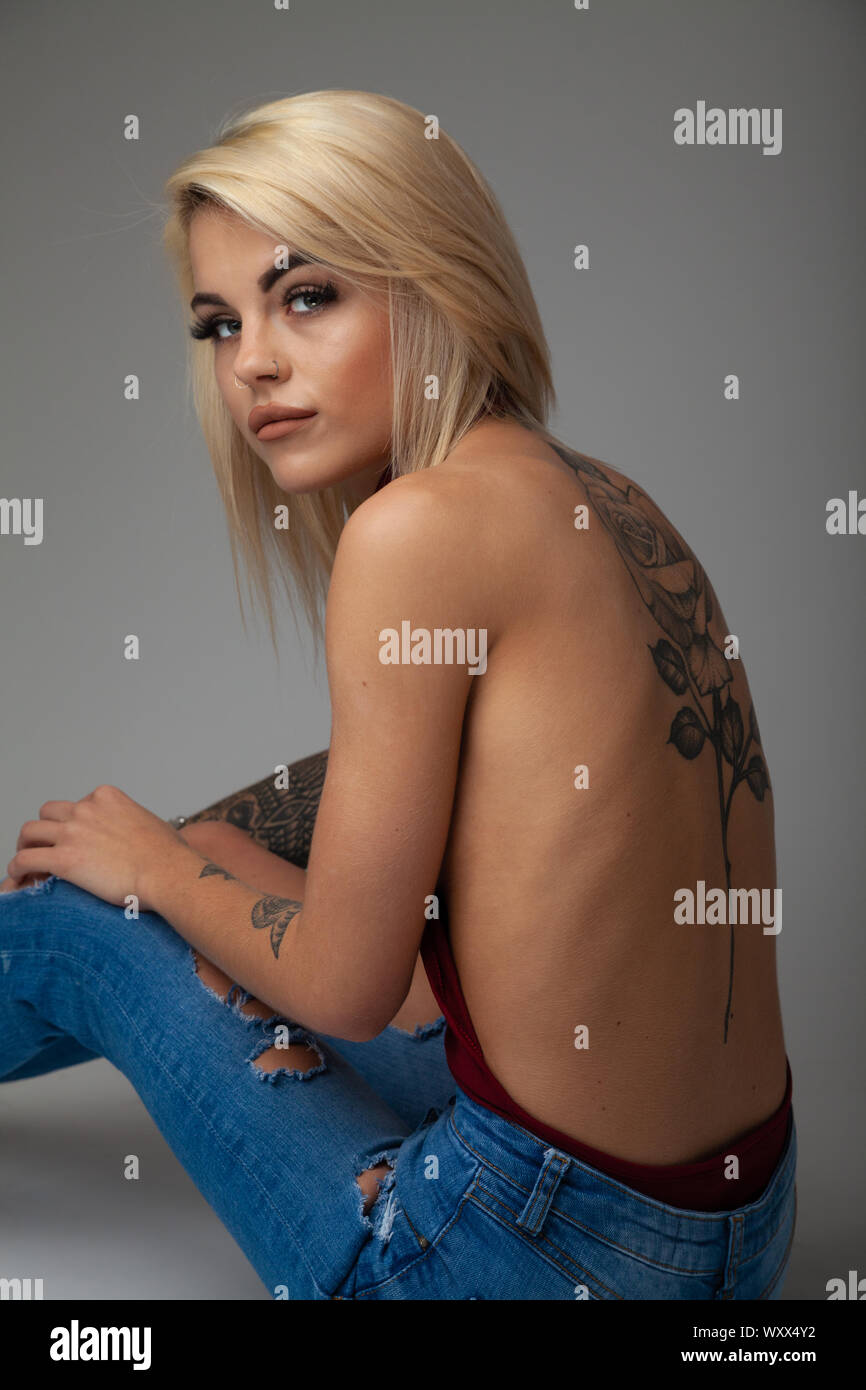 A beautiful young woman with tattoos sitting down with her back towards camera. Stock Photo