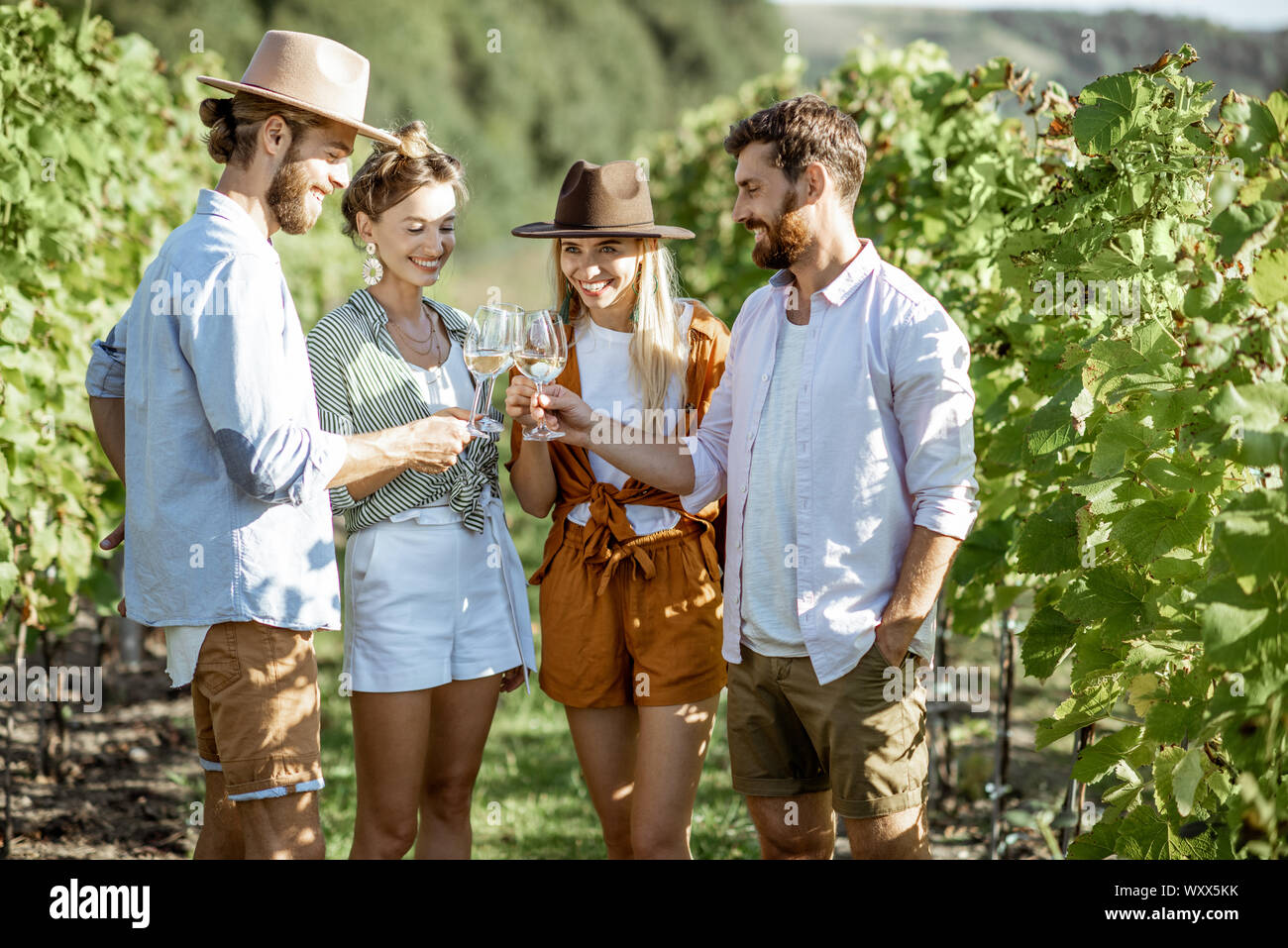 Group of young friends dressed casually hanging out together, tasting wine and clinking glasses on the vineyard on a sunny summer morning Stock Photo