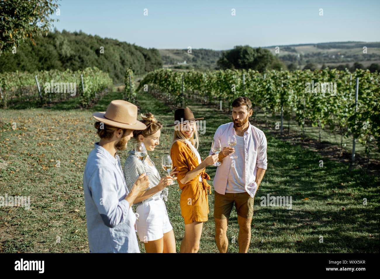 Group of young friends dressed casually having fun together, tasting wine on the vineyard on a sunny summer morning, beautiful landscape view Stock Photo