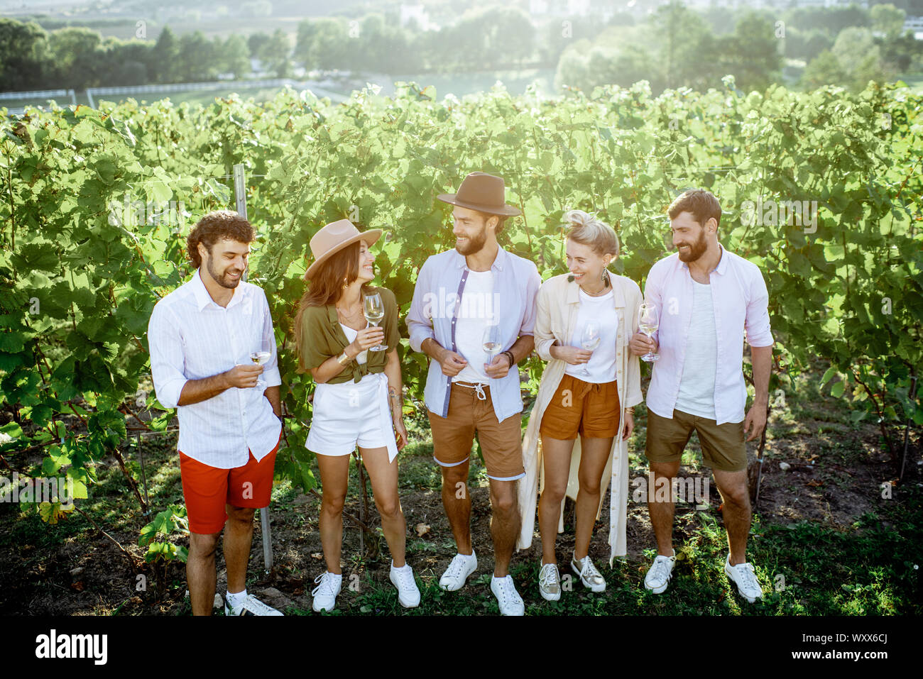 Group of young friends dressed casually hanging out together, tasting wine on the vineyard on a sunny summer morning Stock Photo