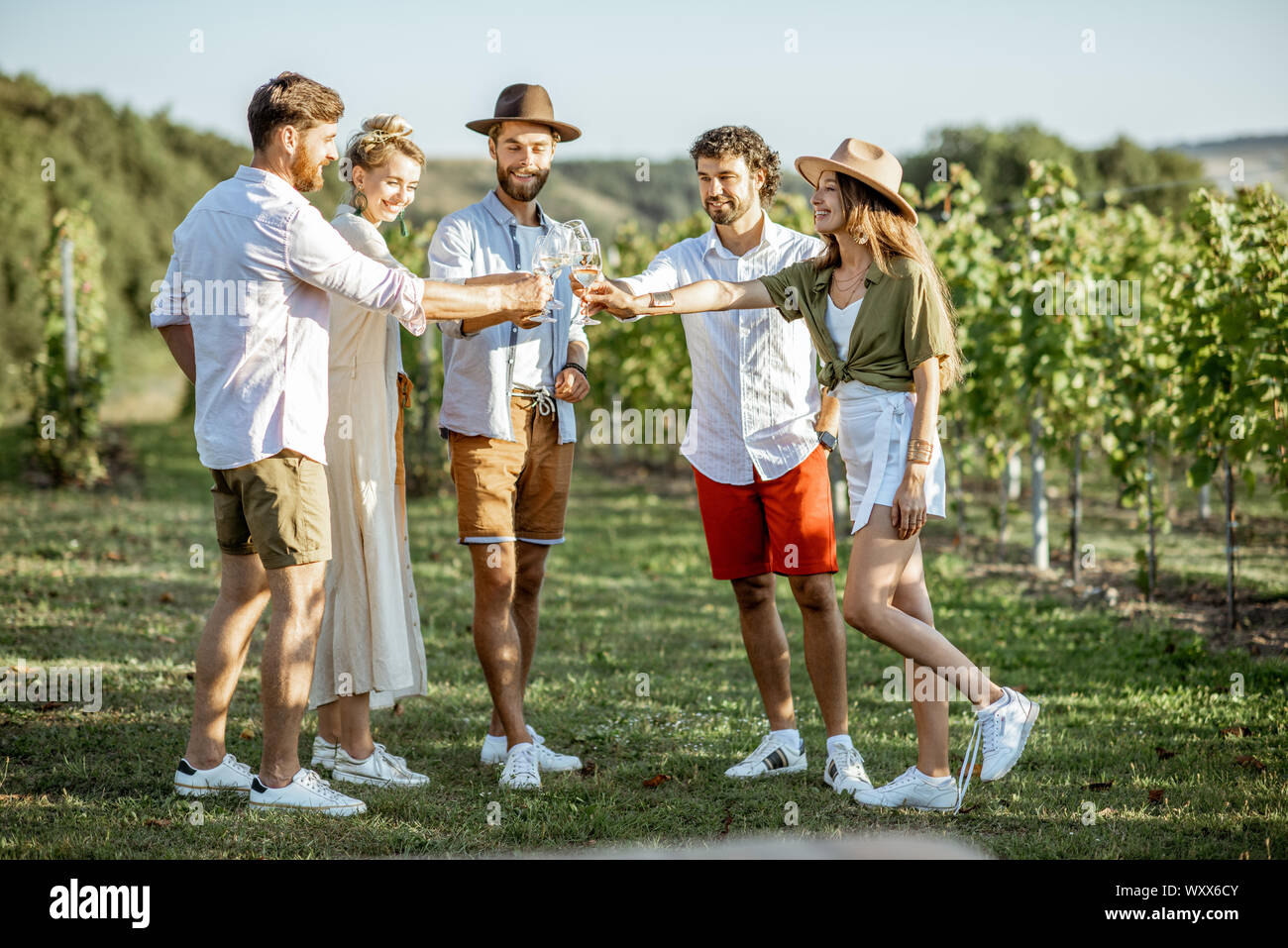 Group of young friends dressed casually hanging out together, tasting wine on the vineyard on a sunny summer morning Stock Photo