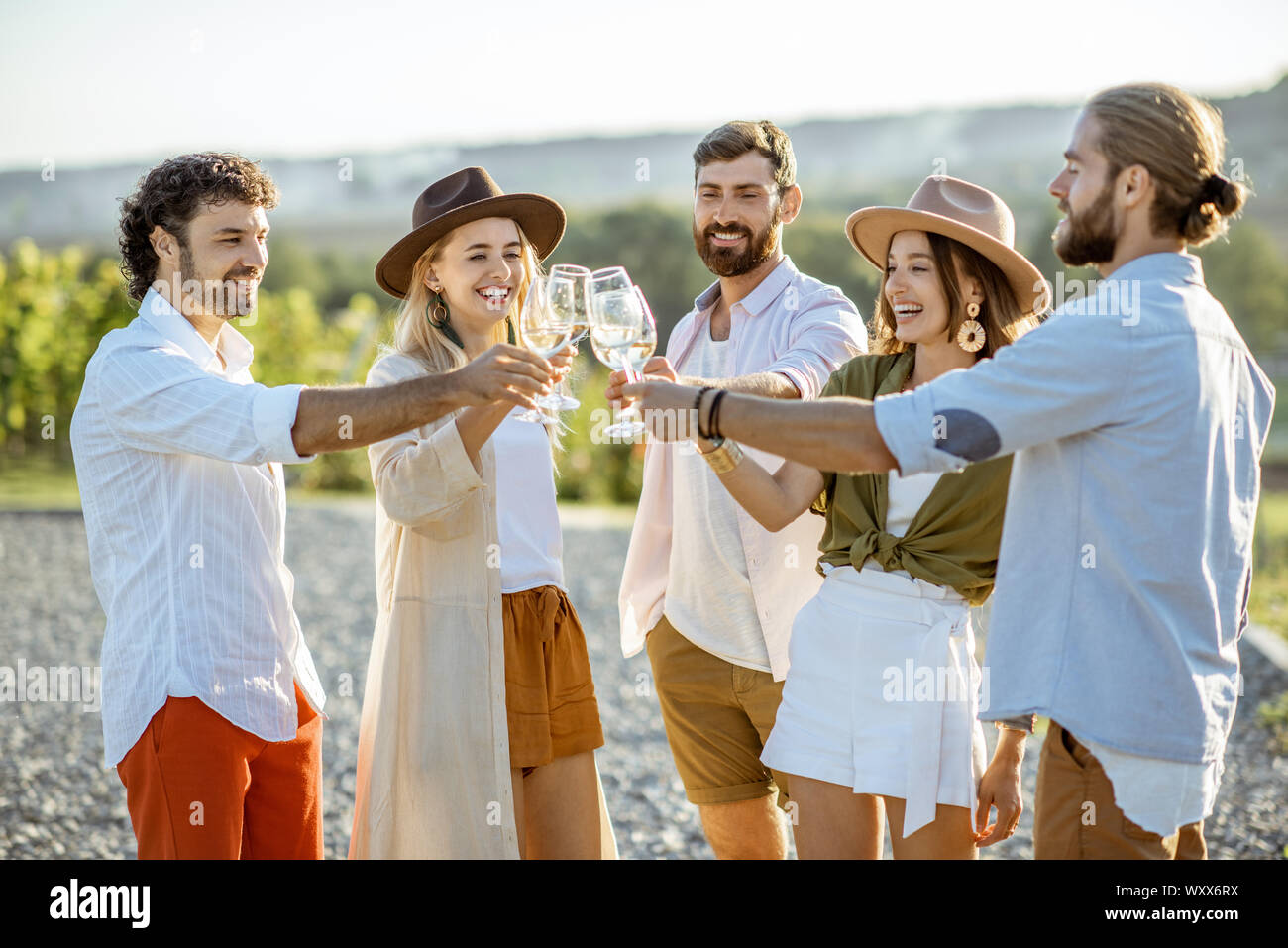 Group of young friends dressed casually hanging out together, tasting wine and clinking glasses on the vineyard on a sunny day Stock Photo