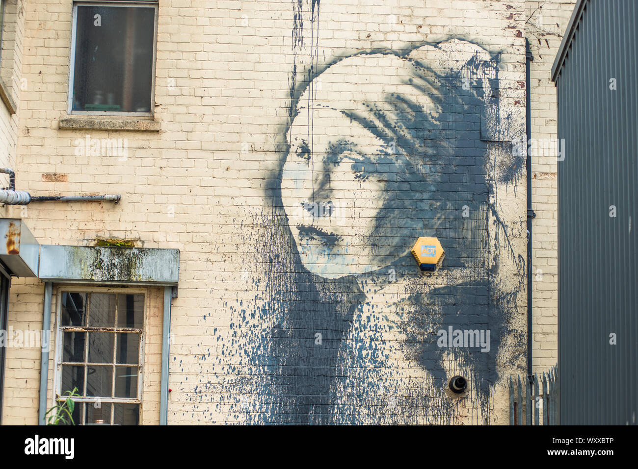 Girl with a pierced eardrum - an artwork based around a burglar alarm by artist Banksy on the wall of an alley in Albion Docks, Bristol, England, UK Stock Photo