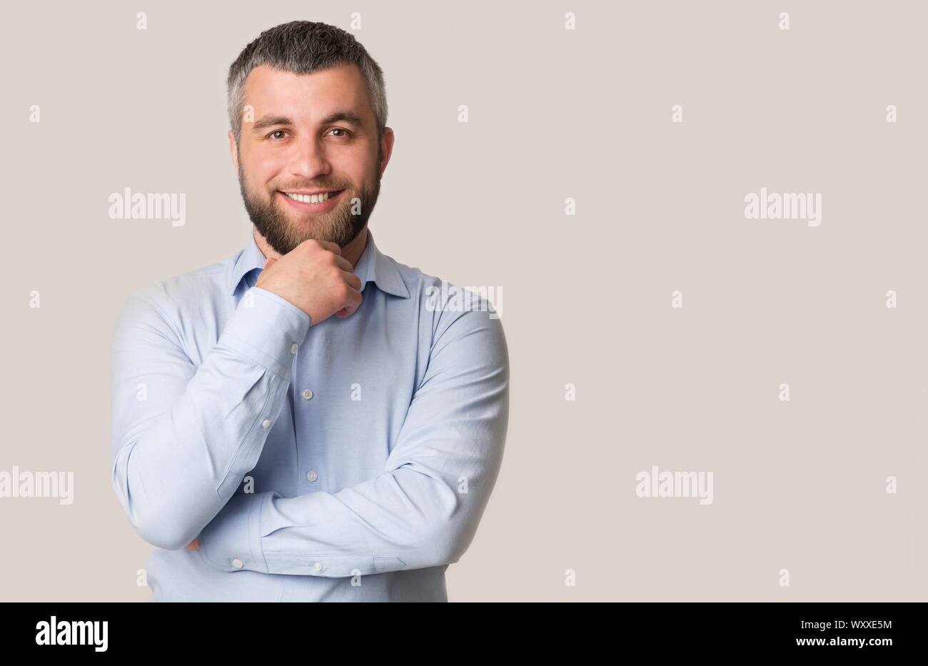 Interested smiling bearded man touching chin over white background Stock Photo