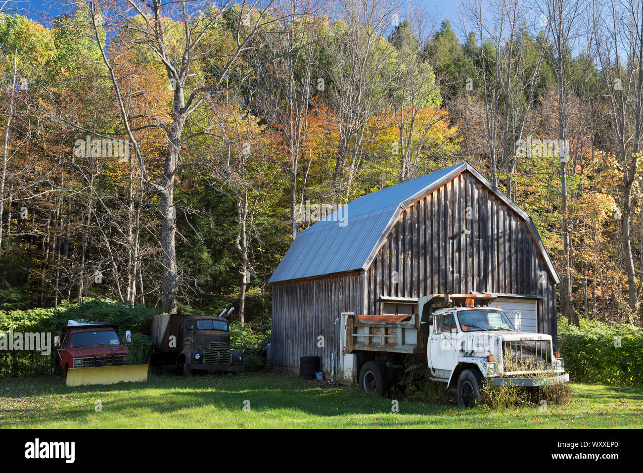 GMC truck and automobiles, one with snow plough, by traditional and typical old barn in Vermont, New England, USA Stock Photo