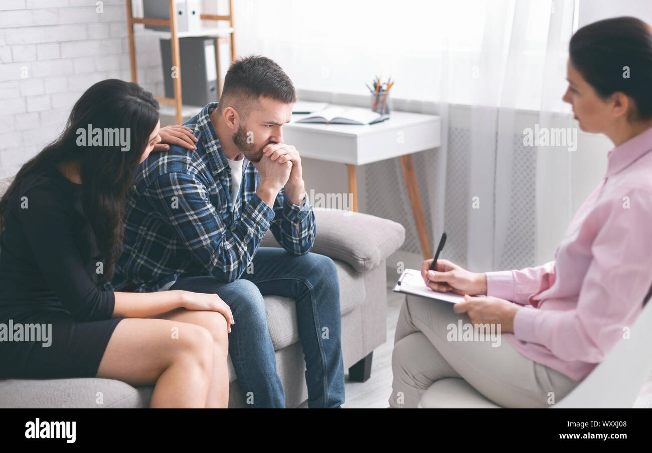 Caring wife comforting her stressed husband at psychological session Stock Photo
