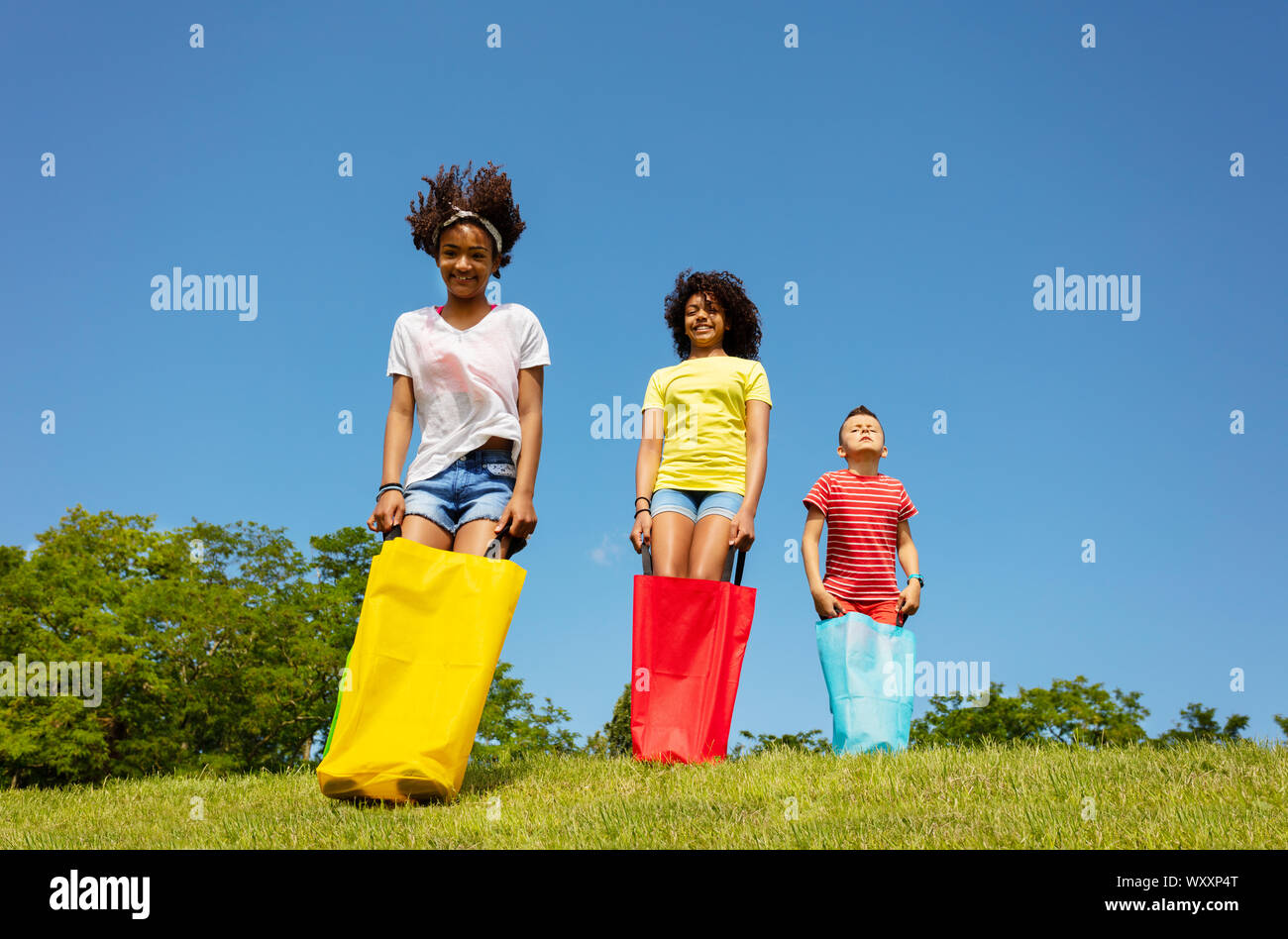 Group of kids play gunny sack race - competitive game on the field, hop forward with smile Stock Photo