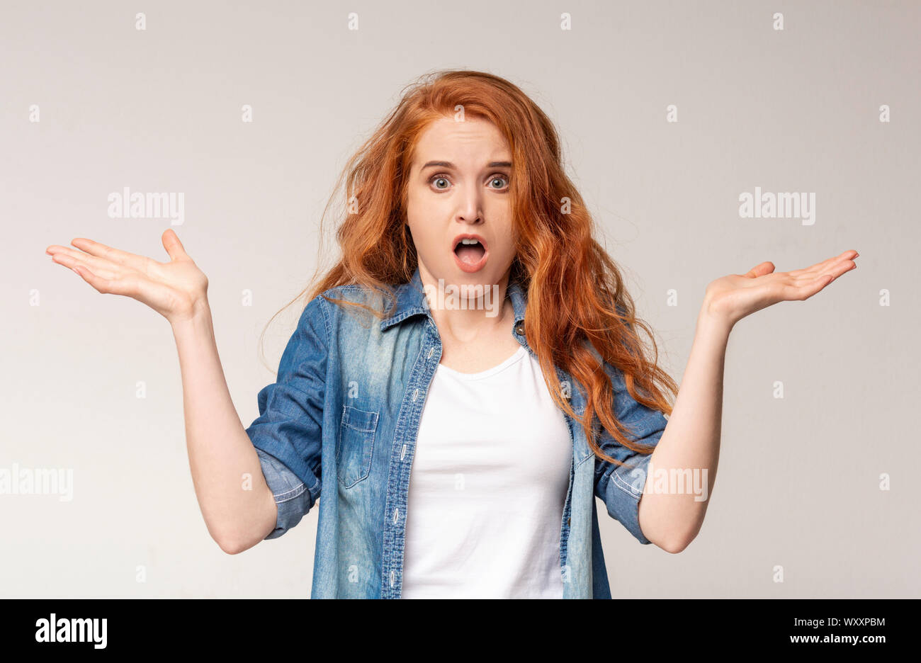 Confused Redhead Girl Shrugging Shoulders On Light Studio Background Stock Photo Alamy