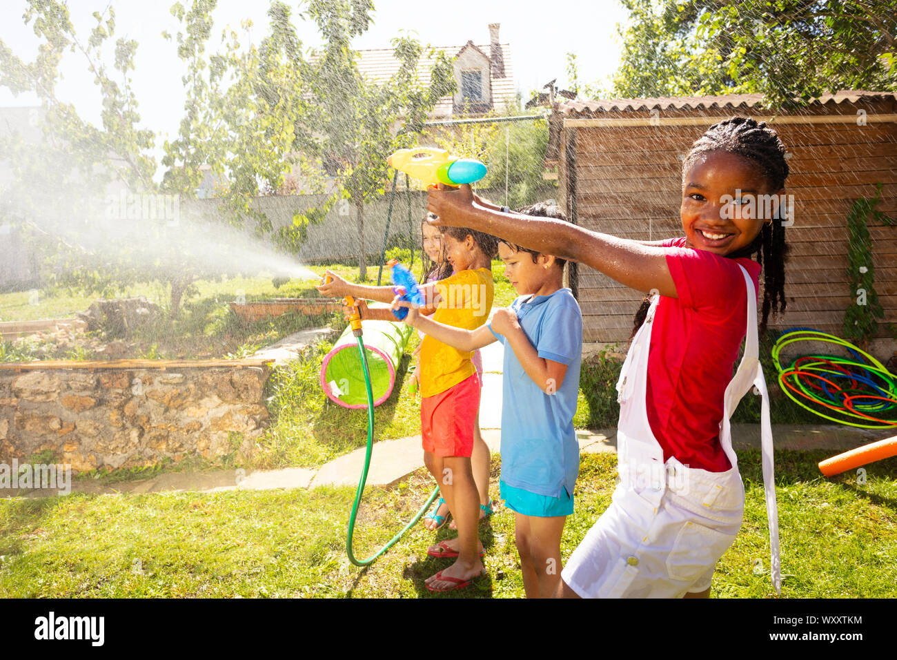 Kids in the middle of water gun fight shooting guns, pistols and garden