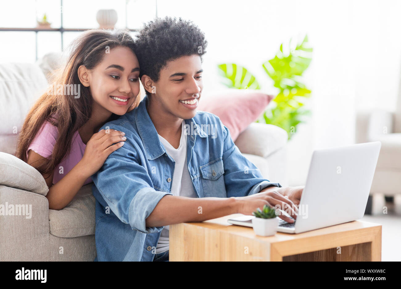 Happy african teen couple working together on laptop at home. Stock Photo