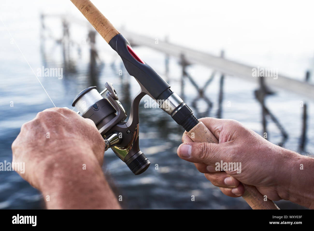 https://c8.alamy.com/comp/WXY03F/the-hands-of-an-adult-man-holding-a-sport-fishing-rod-with-reel-and-line-in-the-background-the-sea-or-a-lake-with-a-wooden-jetty-or-pier-WXY03F.jpg