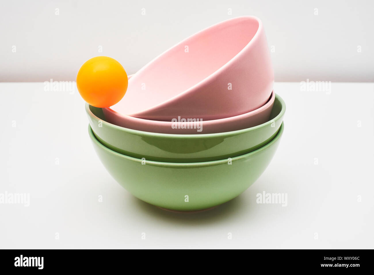 Pink and green earthenware and porcelain bowls, isolated on a white background, on a table or top, with an orange ball balanced on the edge Stock Photo