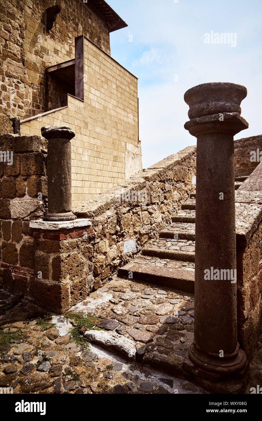 Two ancient stone columns at the foot of an old staircase in a medieval castle with brick walls,  in the municipality of Cellere Stock Photo