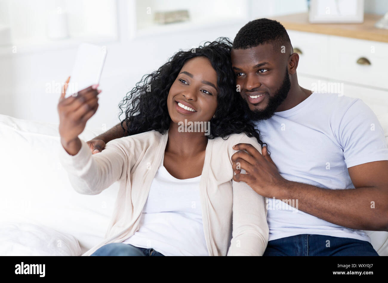 Romantic couple taking selfie while sitting on sofa at home Stock Photo ...